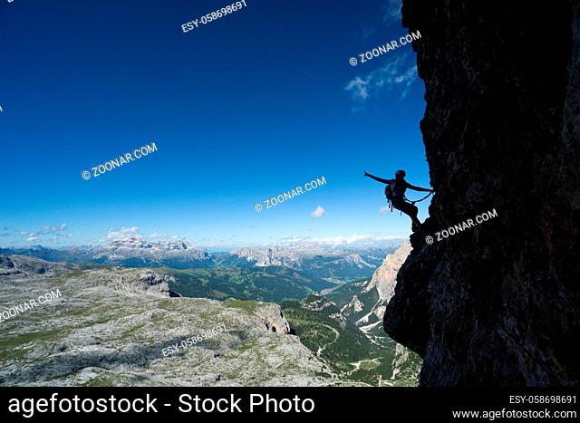Horizontal view of an attractive blonde female climber in silhouette on a steep Via Ferrata pointing to the sky