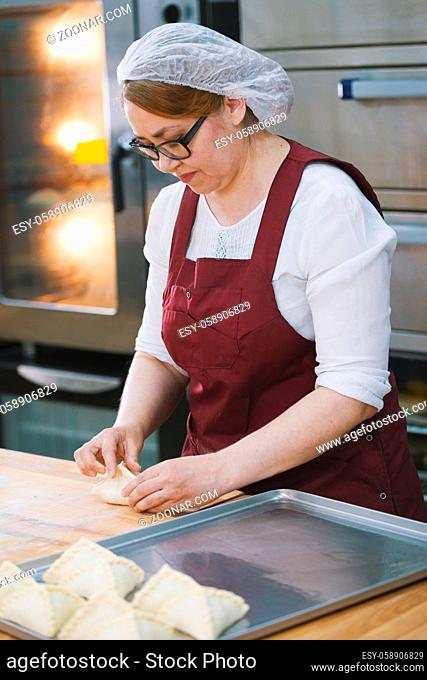 Adult woman in glasses and apron bakes cakes in the bakery half-profile close-up