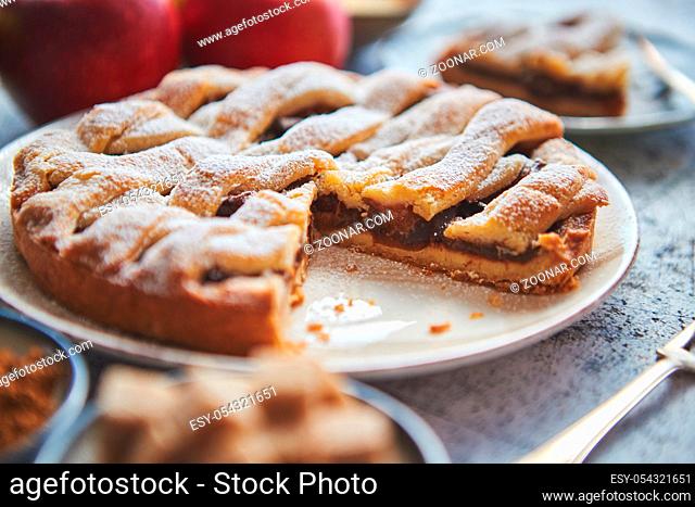 Fresh baked apple pie with cutted slice on small plate. With ingrediends on side. Fresh fruits, brown sugar cubes, cinnamon