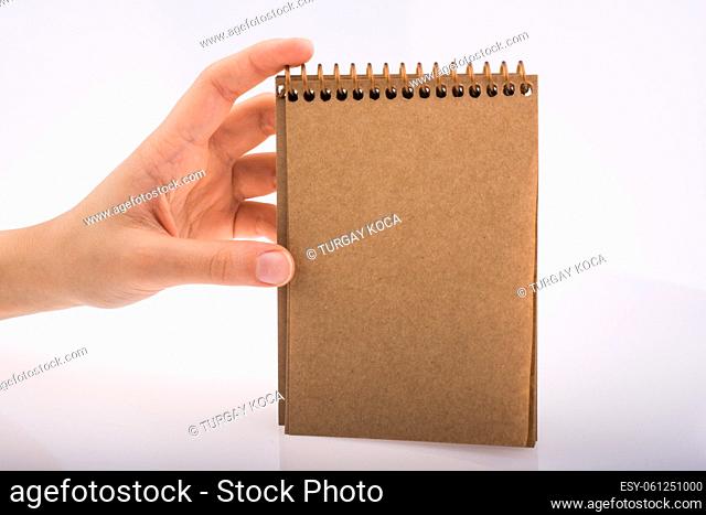Hand holding a brown spiral notebook on a white background