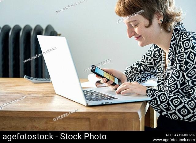 Smiling woman using smartphone and laptop while working from home