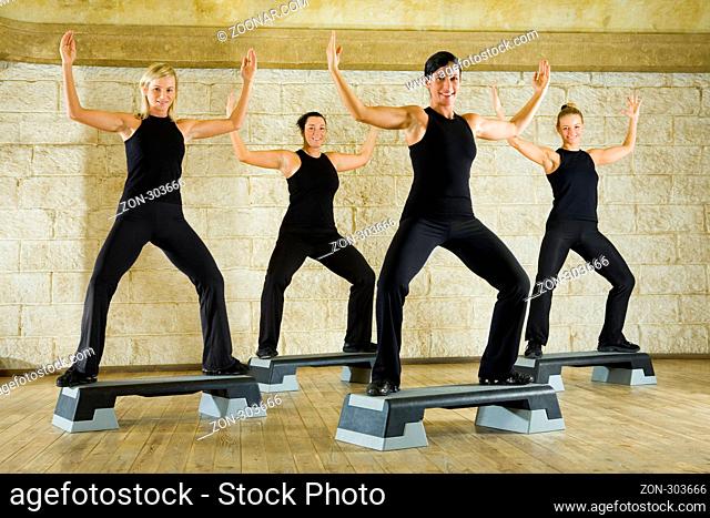 A group of women exercising in the fitness club. They're smiling and looking at camera. They have hands up. Low angle view
