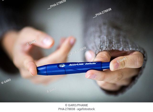 A diabetic person is checking her blood sugar level (self glycemia). A drop of blood obtained with a pen-like lancing device is placed on a test stick and...