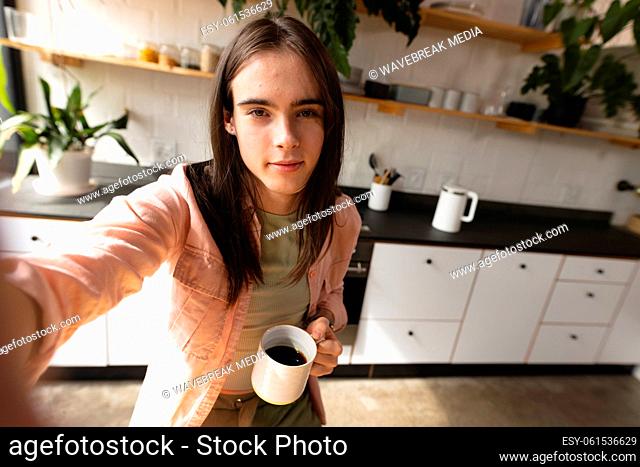 Portrait of non-binary trans woman holding a coffee cup looking at the camera in the kitchen at home