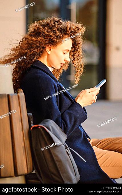 Young woman sits on bench and looking for apartment for rent in modern city