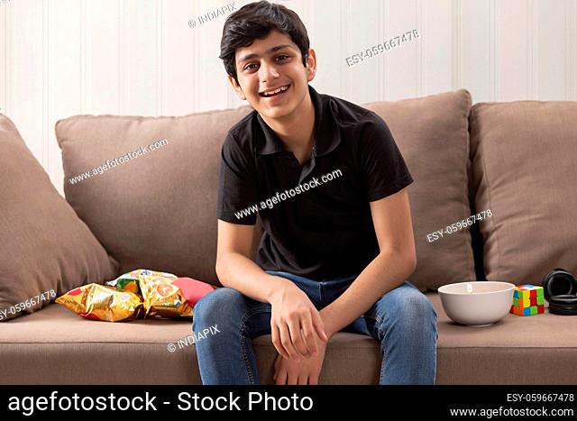 A TEENAGE BOY HAPPILY LOOKING AT CAMERA WHILE SITTING WITH SNACKS