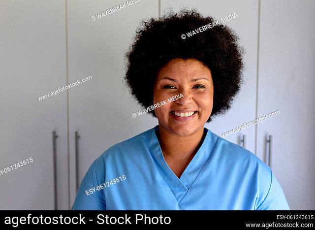 Portrait of smiling african american mid adult female nurse standing against cabinet in hospital