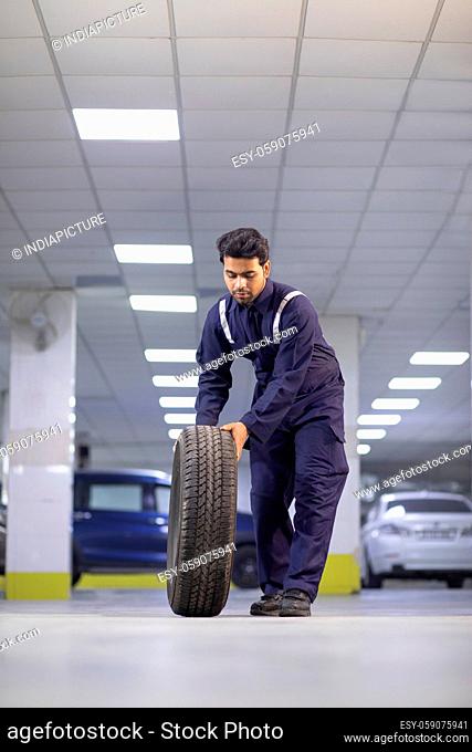 Full-length Mechanic carrying a tire at motor garage