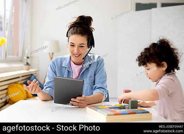 Mother working from home using digital tablet while daughter is playing with buiilding blocks