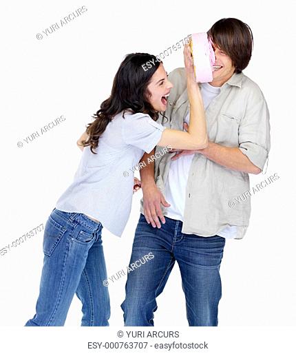 Cheerful young girl smashing cake on a guy's face over white background