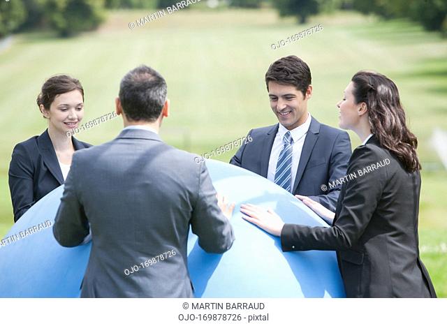 Business people standing outdoors with large ball