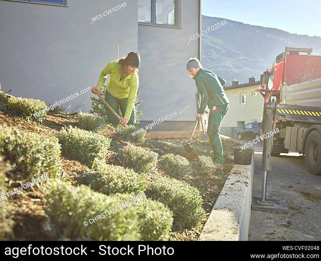 Young gardeners digging mud outside building on sunny day