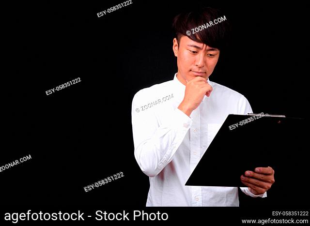 Studio shot of young handsome Asian businessman against black background