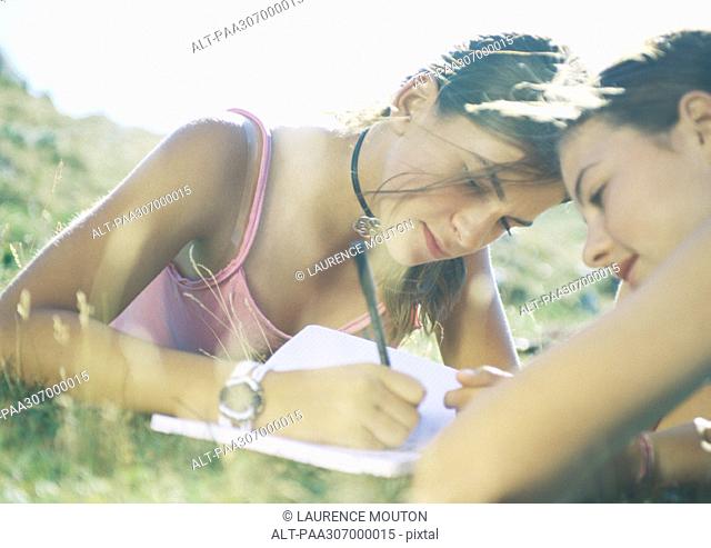 Two girls lying in grass, one writing