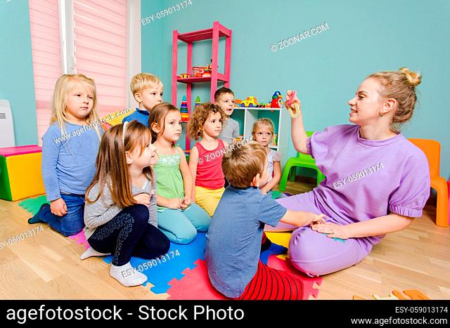Group of lovely kids sitting on a floor in front of teacher and listen attentively. Preschoolers learning to count