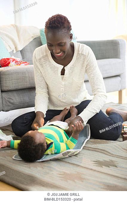 Black mother changing diaper of baby boy in living room