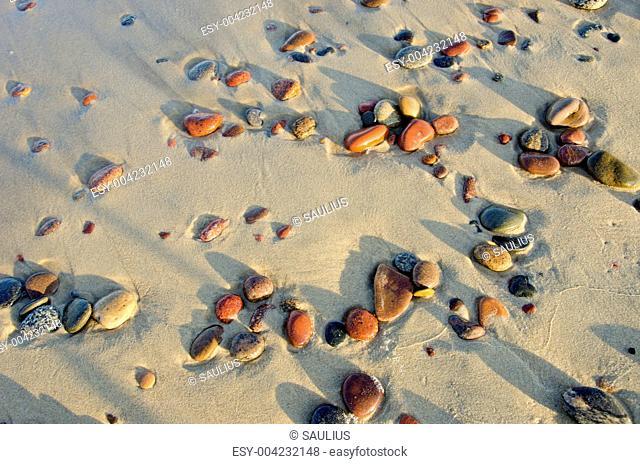Colorful wet pebbles rubed by waves in sea sand