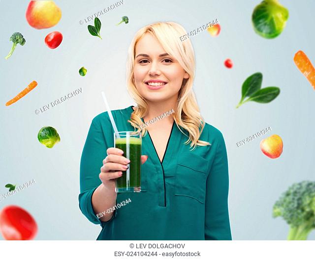 healthy eating, vegetarian food, diet, detox and people concept - smiling young woman drinking green vegetable juice or smoothie from glass over blue sky and...