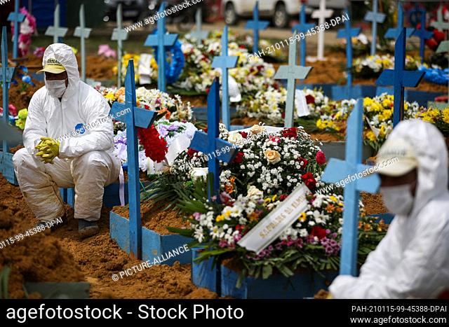 15 January 2021, Brazil, Manaus: Cemetery workers in protective suits sit on graves decorated with flowers during a funeral at Nossa Senhora Aparecida Cemetery