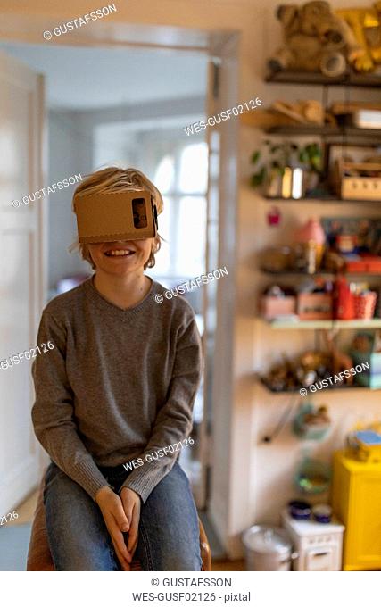 Boy sitting on buck in his room at home wearing cardboard VR glasses