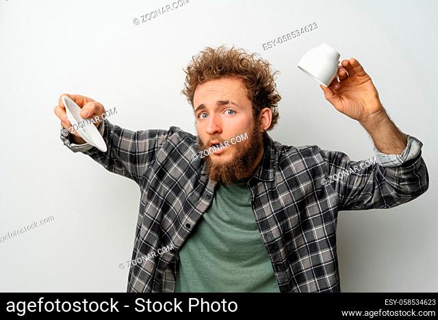 No coffee in inverted cup good looking man with curly hair and beard holding cup, wearing plaid long sleeve shirt isolated on white background