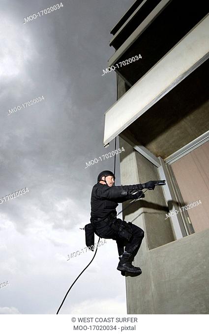 SWAT Team Officer Rappelling and Aiming Gun