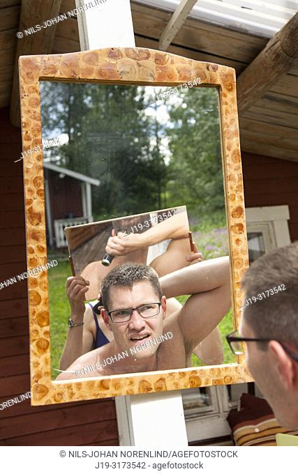 Young man trimming his hair in mirror, northern Sweden