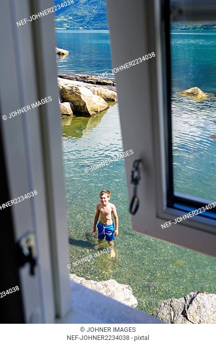 Boy standing in sea seen from the window