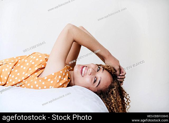 Smiling woman with hand in hair lying on bed at home