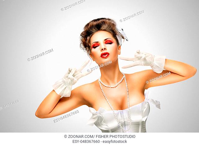 Sexy pinup bride in a vintage wedding corset showing V sign on grey background