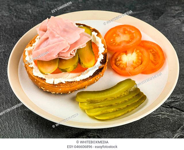Ham Tomato and Cheese Spread Sesame Bagel With Gherkins Against a Black Background