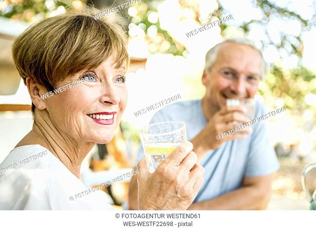Smiling senior woman drinking glass of water with husband in background