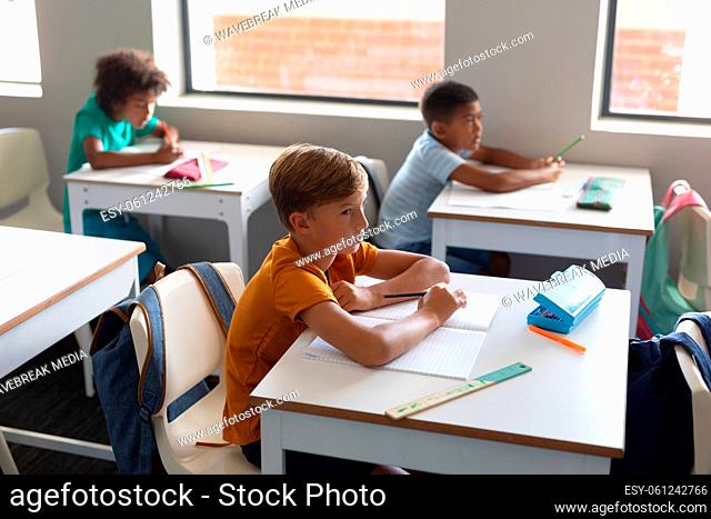 Multiracial elementary students looking away while sitting at desk in classroom