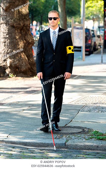 Blind Man Walking On Sidewalk Holding Stick Wearing Armband