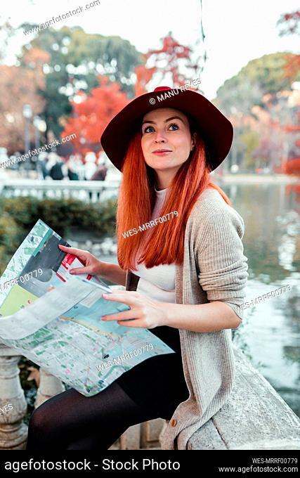 Beautiful woman wearing hat holding map while sitting in park