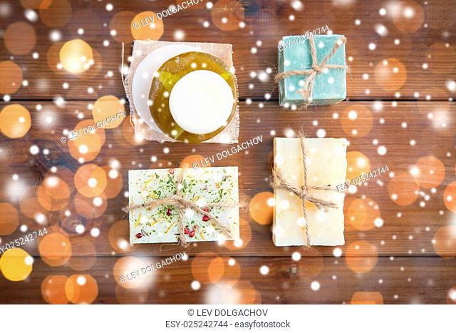 beauty, spa, bodycare, bath and natural cosmetics concept - handmade soap bars on wooden table over lights and snow