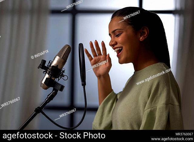A YOUNG WOMAN HAPPILY RECORDING MUSIC ON MICROPHONE