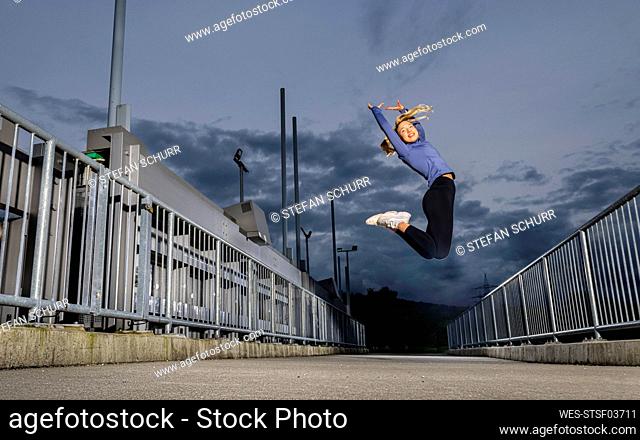 Cheerful athlete jumping with arms raised on river weir