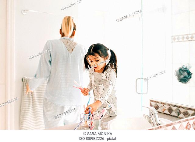 Girl with mother selecting toothbrush in bathroom
