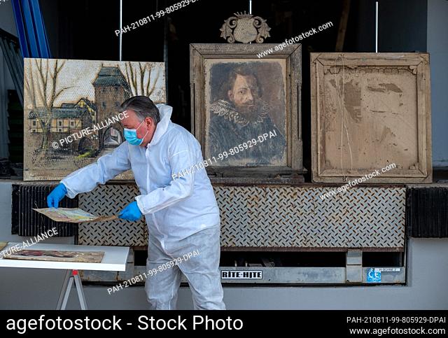 11 August 2021, Rhineland-Palatinate, Trier: Painting restorer Dimitri Scher lines up one of the paintings rescued from the flood on a table