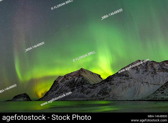 Strong aurora over the mountains at Haukland beach in winter, Lofoten