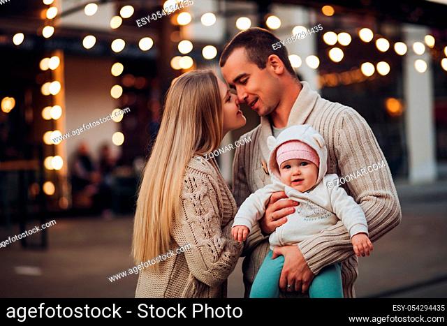 Portrait of young happy family standing together in cosiness atmosphere. Handsome man in sweater holding little smiling baby on hands