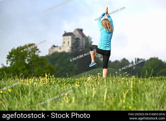 03 May 2020, Baden-Wuerttemberg, Waldburg: Qi Gong teacher Elisabeth does some exercises in the morning, while in the background the castle Waldburg is...