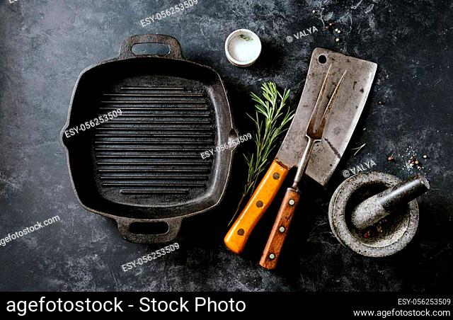 Vintage Meat cleaver with fork and cast iron pan on a dark background. Top view, space for text