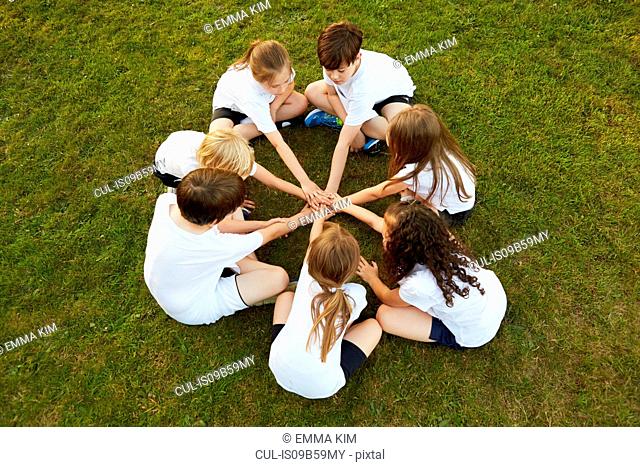 Overhead view of boy and girl sport team sitting on grass in circle on playing field