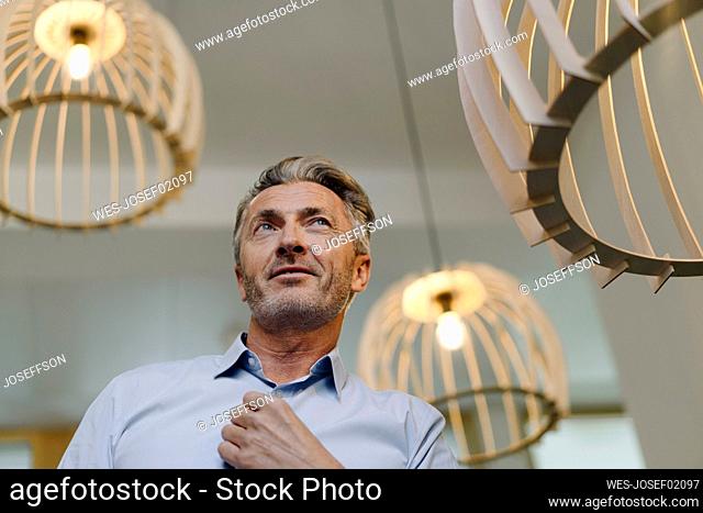 Businessman standing by illuminated light fixture at office