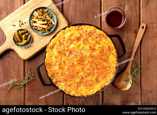 Homemade Shepherd's pie in a cooking pan with pickles and wine, shot from the top on a dark rustic wooden background