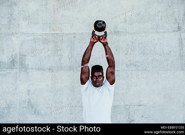 Young sportsman exercising with kettle bell against white wall