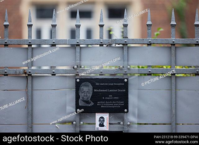 PRODUCTION - 18 December 2023, North Rhine-Westphalia, Dortmund: Posters and a plaque at the crime scene (behind the fence) commemorate 16-year-old Senegalese...