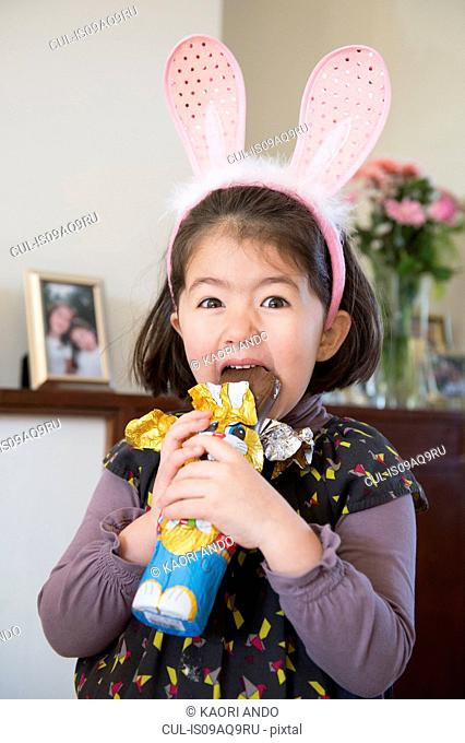 Young girl wearing bunny ears, just about to bite into chocolate bunny